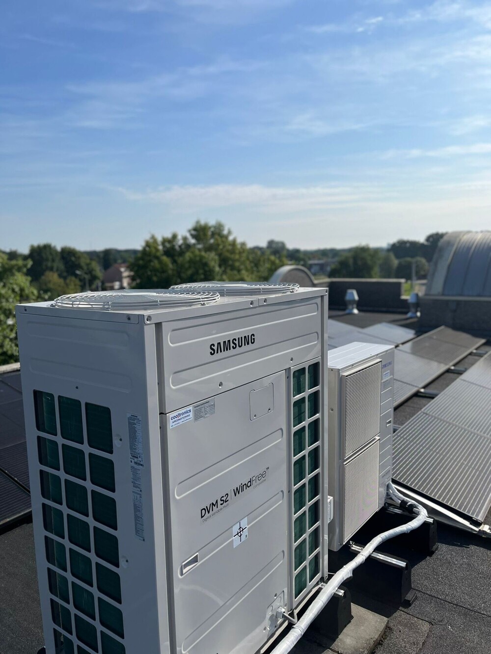 Buitendeel van een warmtepomp naast zonnepanelen op een plat dak